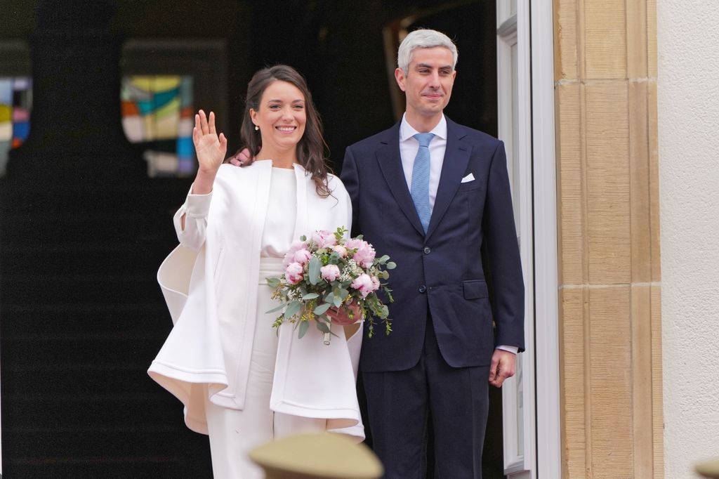 woman waving in white outfit with man in suit 