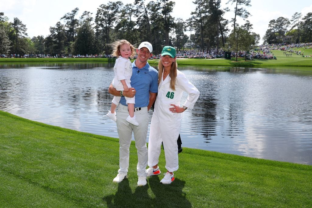 Rory McIlroy holding a young girl alongside his wife Erica Stoll in front of a lake on a golf course