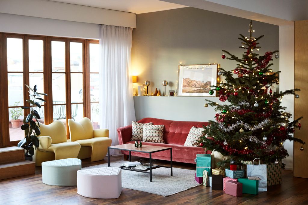 Decorated Christmas tree and gifts by sofa. Interior of living room with furniture. Ottoman stools and chairs by coffee table.