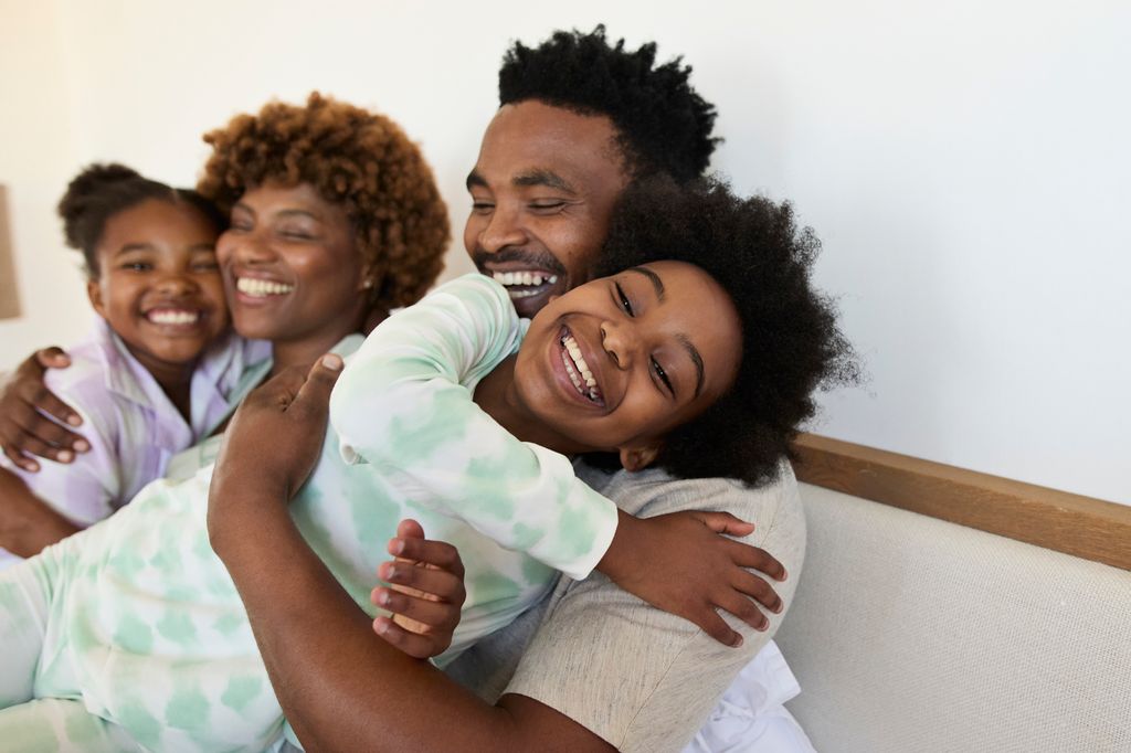 Happy parents embracing daughters on bed at home