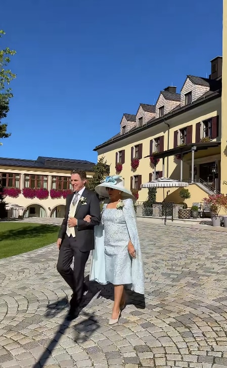 Joan in her powder blue look walking on arm of son in suit