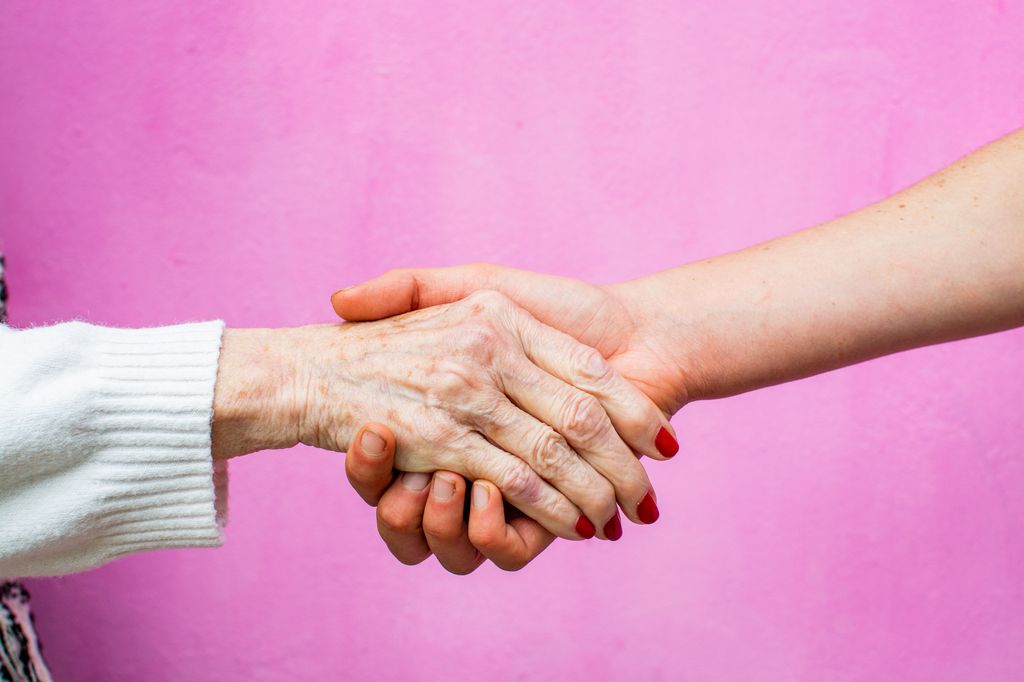 elderly woman giving a handshake to a young woman, pink background