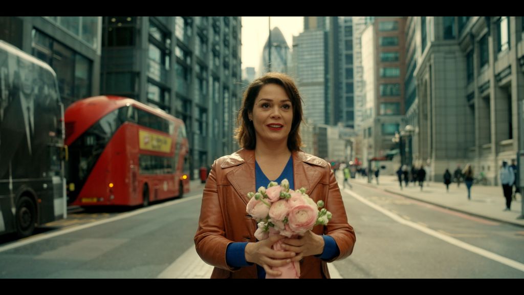 Lola Dewaere as Charlie Holmes. She is seen holding a bouquet of pink flowers. 