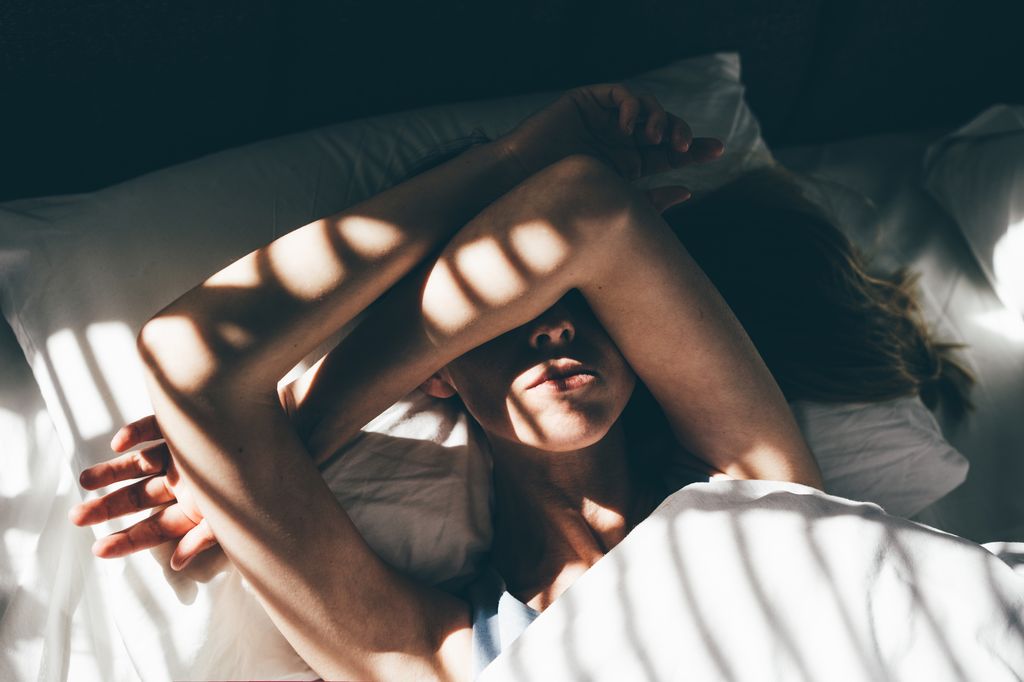 woman in bed with hands across face