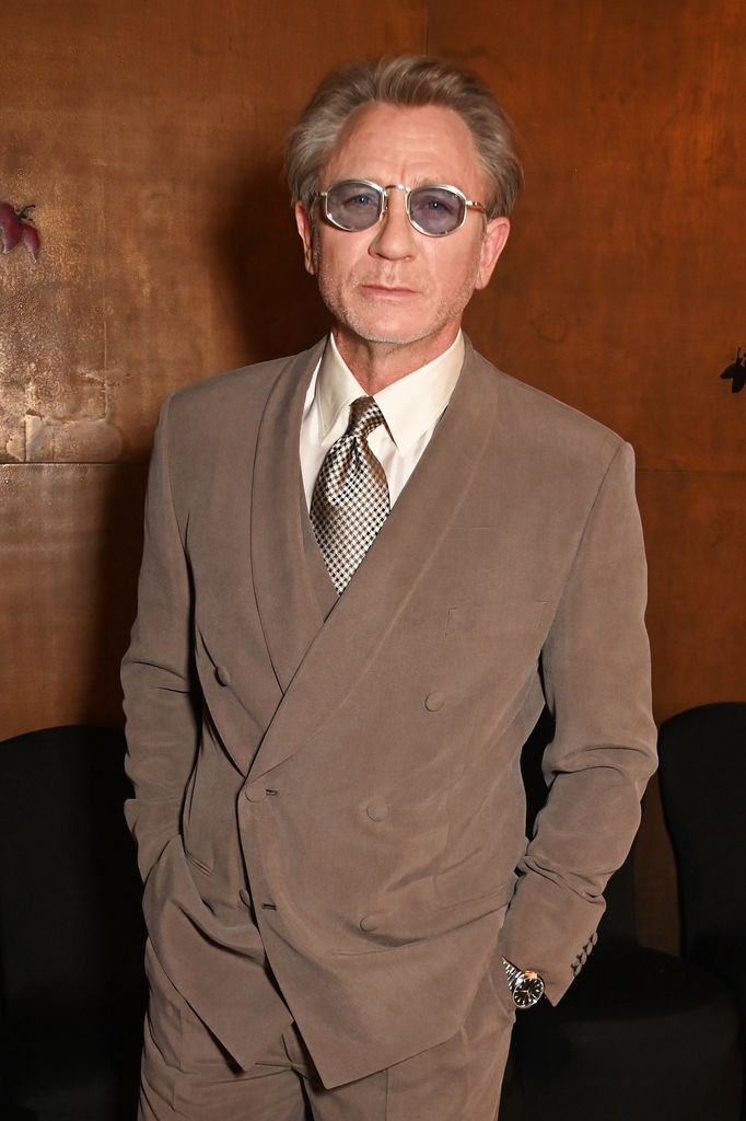 man posing in brown suit and blue tinted glasses