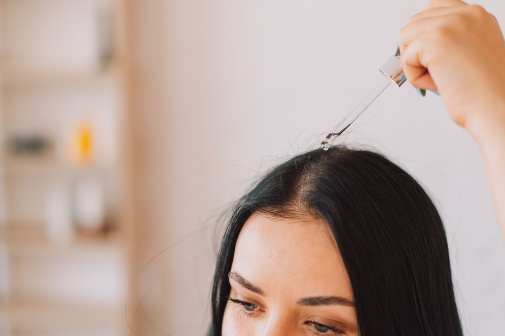 Lady applying serum on scalp and hair from pipette.