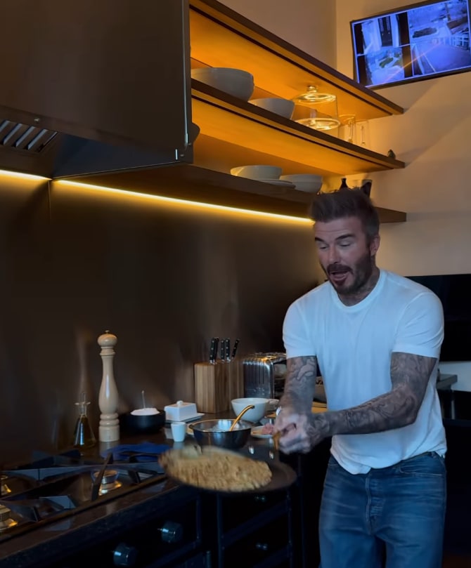 David Beckham holding out a frying pan while flipping a pancake in his kitchen at home