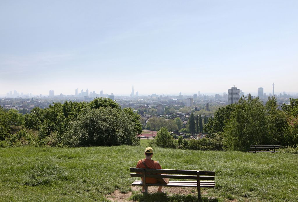 Man sitting on bench reading book and enjoying London skyline from parliament hill.