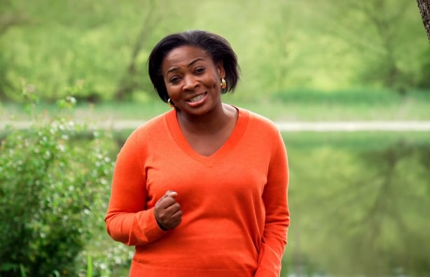 Woman in orange jumper in front of green fields