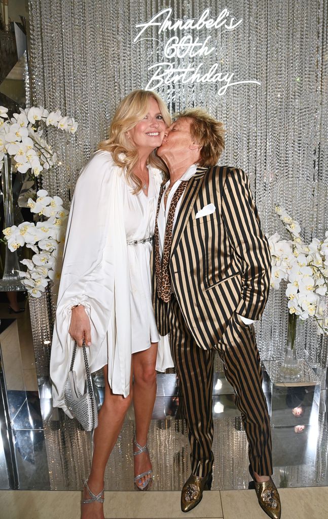 Penny Lancaster getting a kiss from husband Rod Stewart while posing against Happy Birthday sign