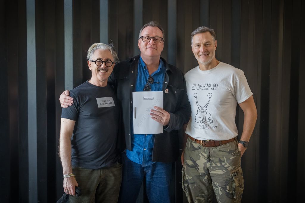 three men standing together, one holding script