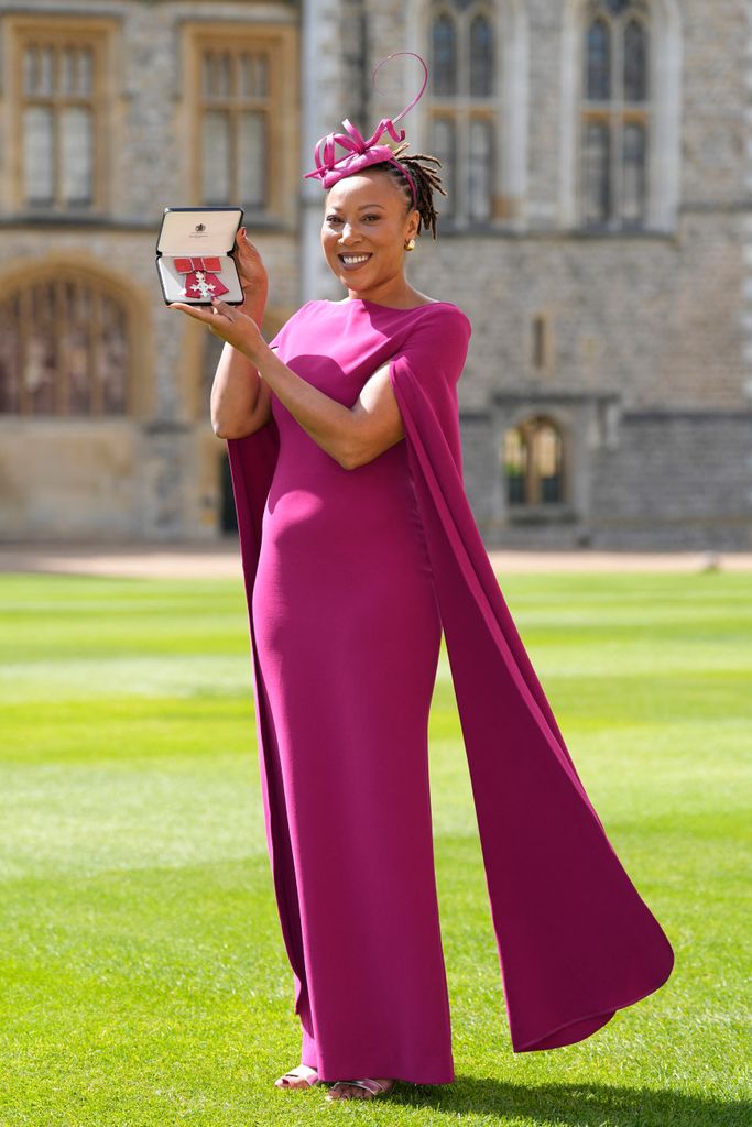 woman holding up her MBE in long maroon dress