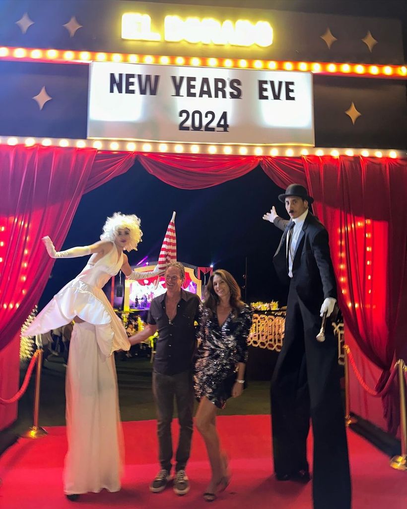 Cindy Crawford and Rande Gerber poses next to man and woman on stilts as they walk into NYE party
