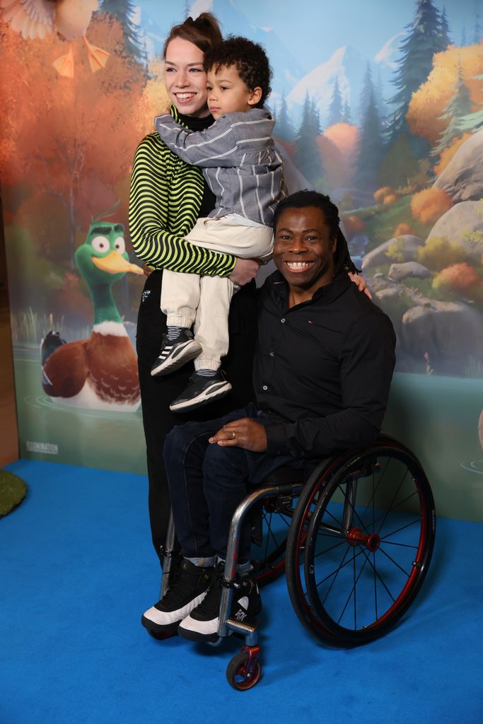 Ade Adepitan and Linda Harrison, who carries a young boy, in front of a movie poster