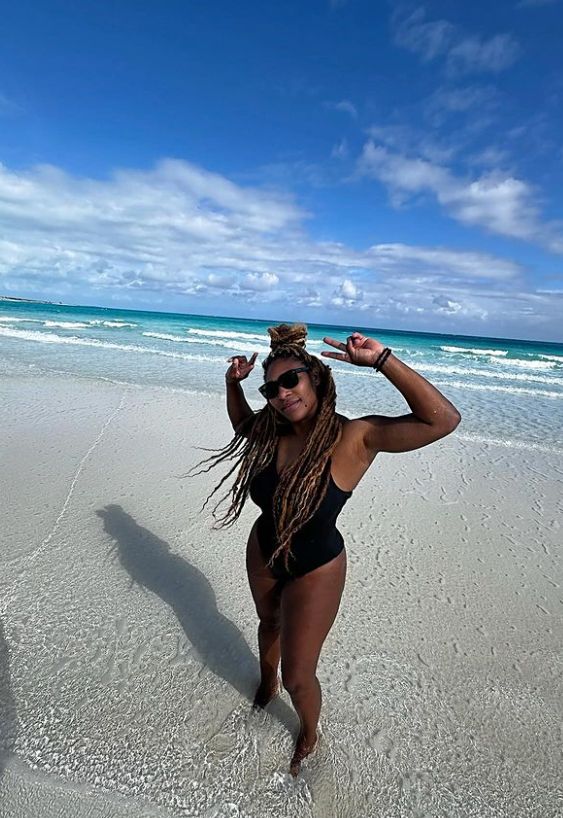 Serena Williams posing on the beach in a black one-piece swimsuit