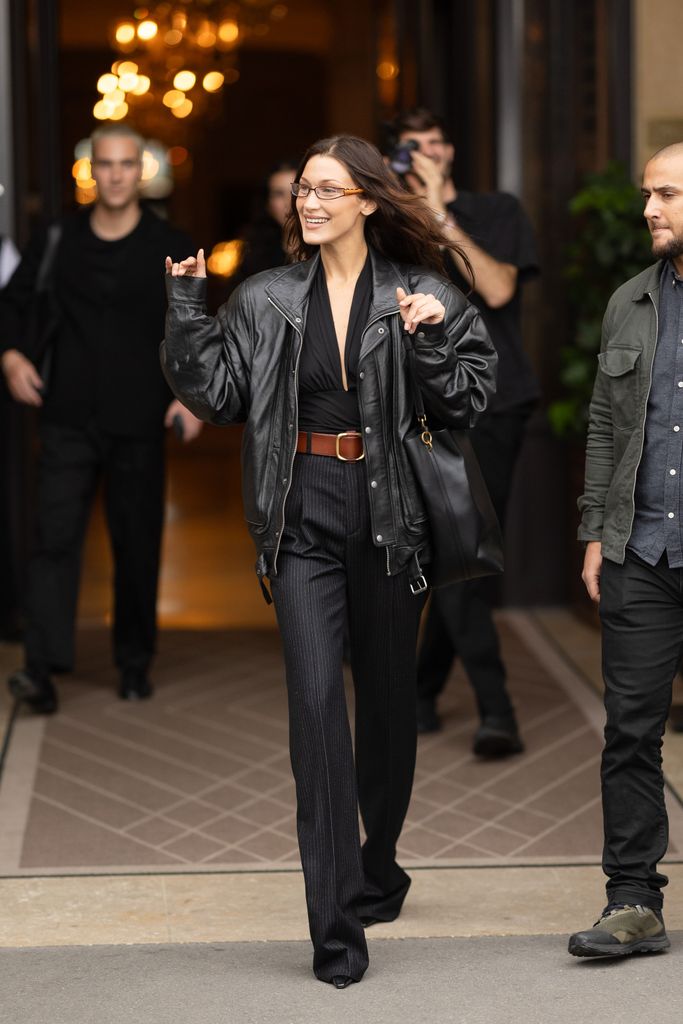 Bella Hadid waving in pinstripe pants and bomber jacket