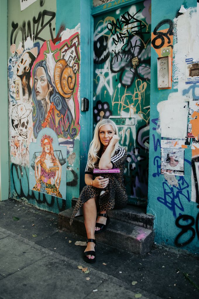 Francesca poses with her book in front of a door full of graffiti