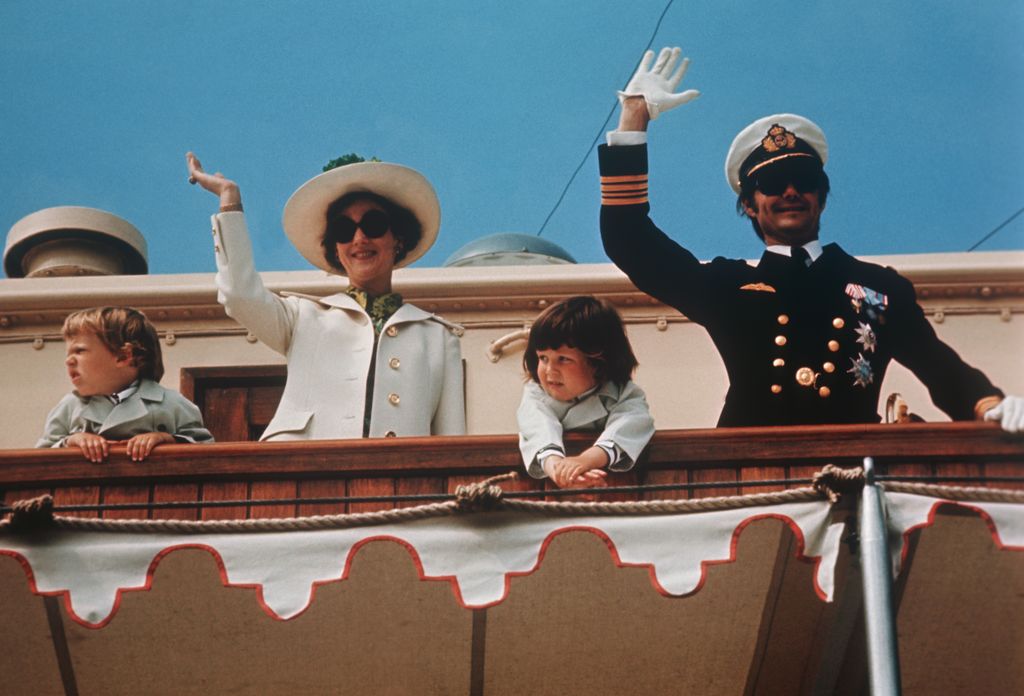 A young Prince Joachim and King Frederik with their parents Queen Margrethe and Prince Henrik waving from a yacht