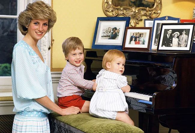 Princess Diana stands at a piano with Princes William and Harry in 1985