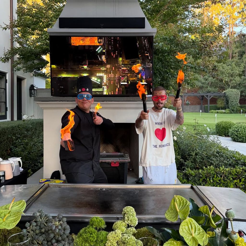 Justin Bieber and a chef holding up torches in front of massive grill outside in his garden in beverly hills