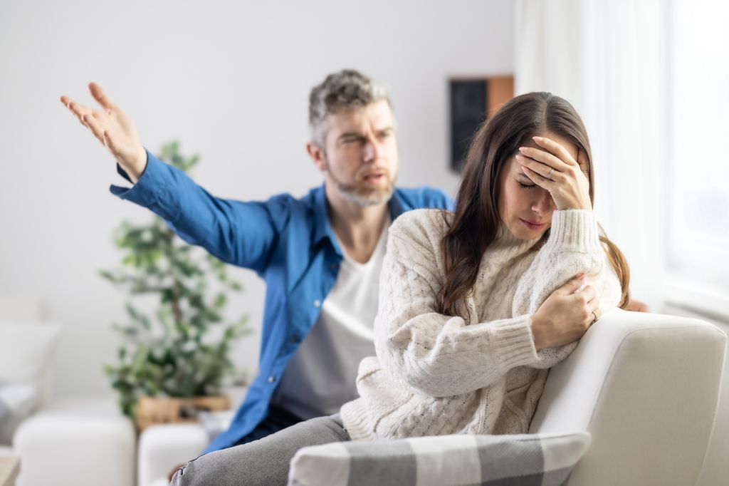 The husband shouts at the partner, who ignores him and holds her head in frustration