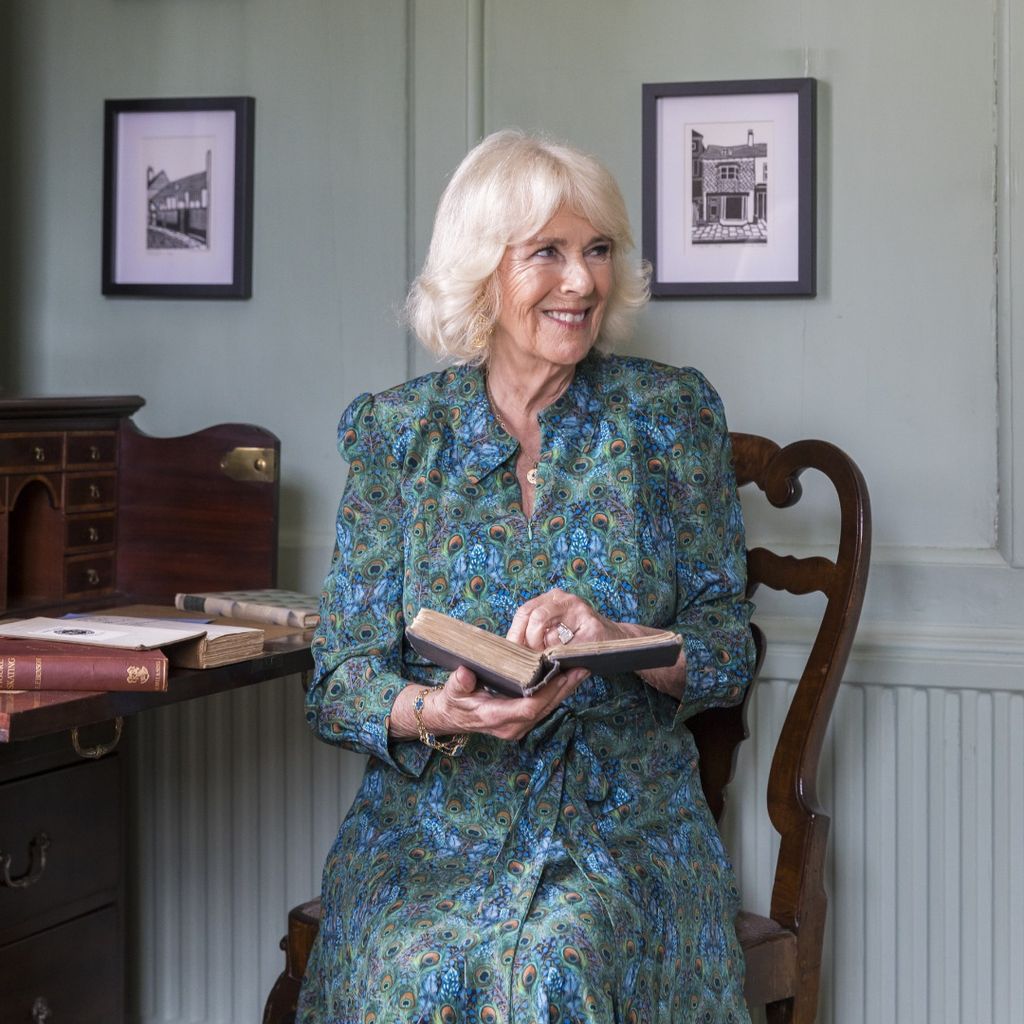 Queen Camilla in a peacock print dress reading a book 