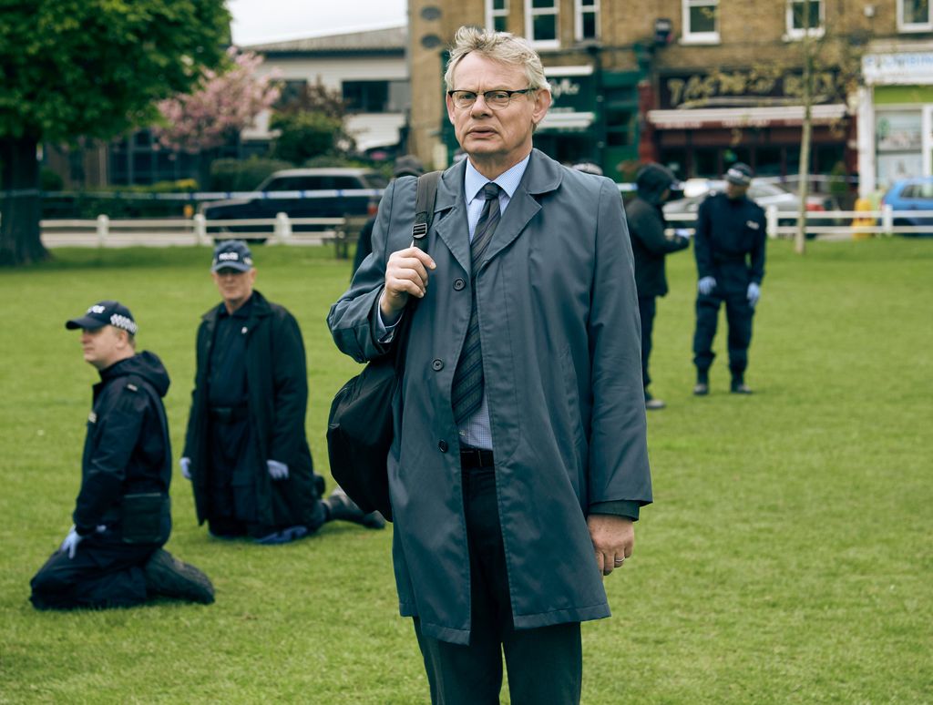 detective standing in field surrounded by police officers