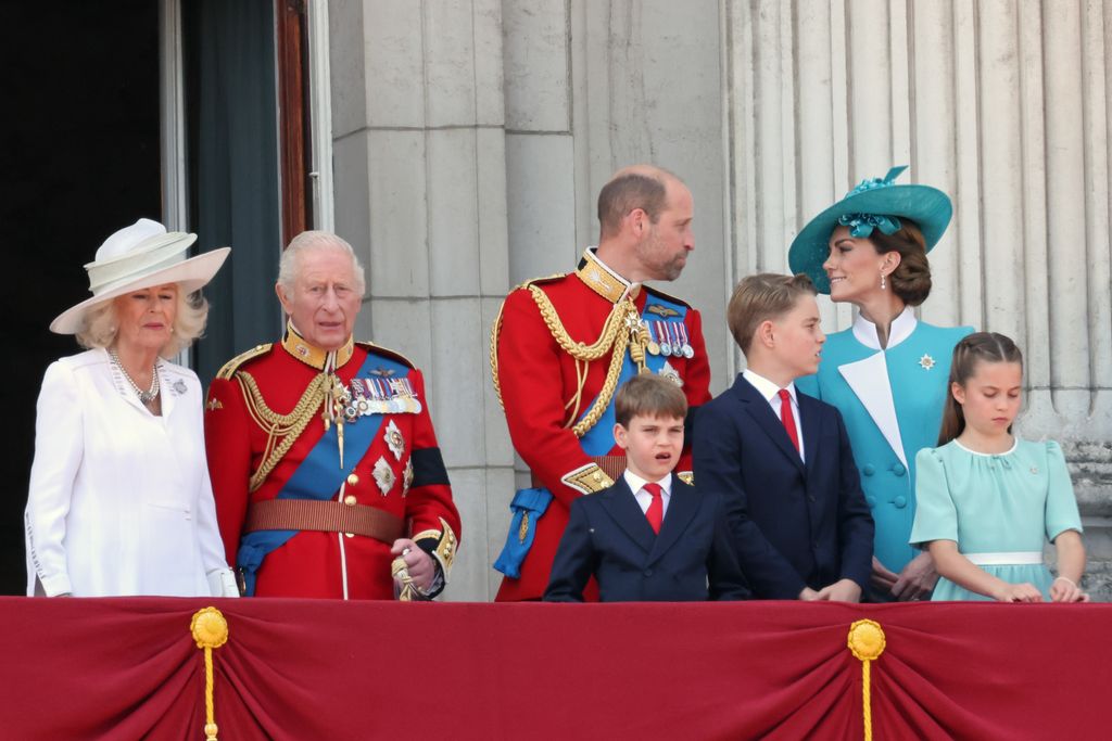 Queen Camilla and King Charles standing close to Prince William, Prince Louis, Prince George, Kate Middleton and Princess Charlotte; William and Kate exchange a loving look