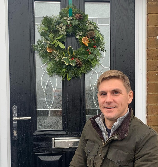 man outside black front door with wreath on