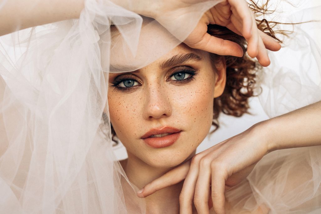 A captivating portrait of a freckled woman with tousled curls while holding a bridal veil
