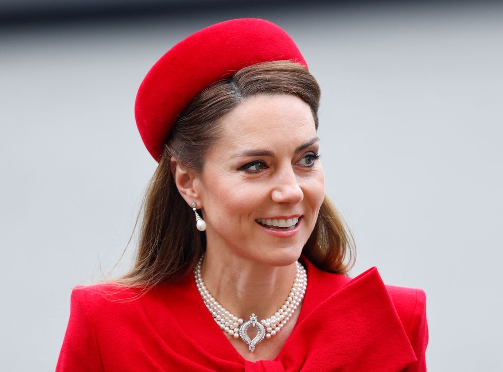 The Princess of Wales in red coat dress and hat smiling for camera while attending Commonwealth Day Service
