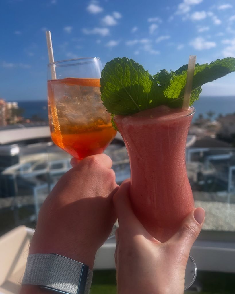 two hands cheersing cocktails against a sunny sky