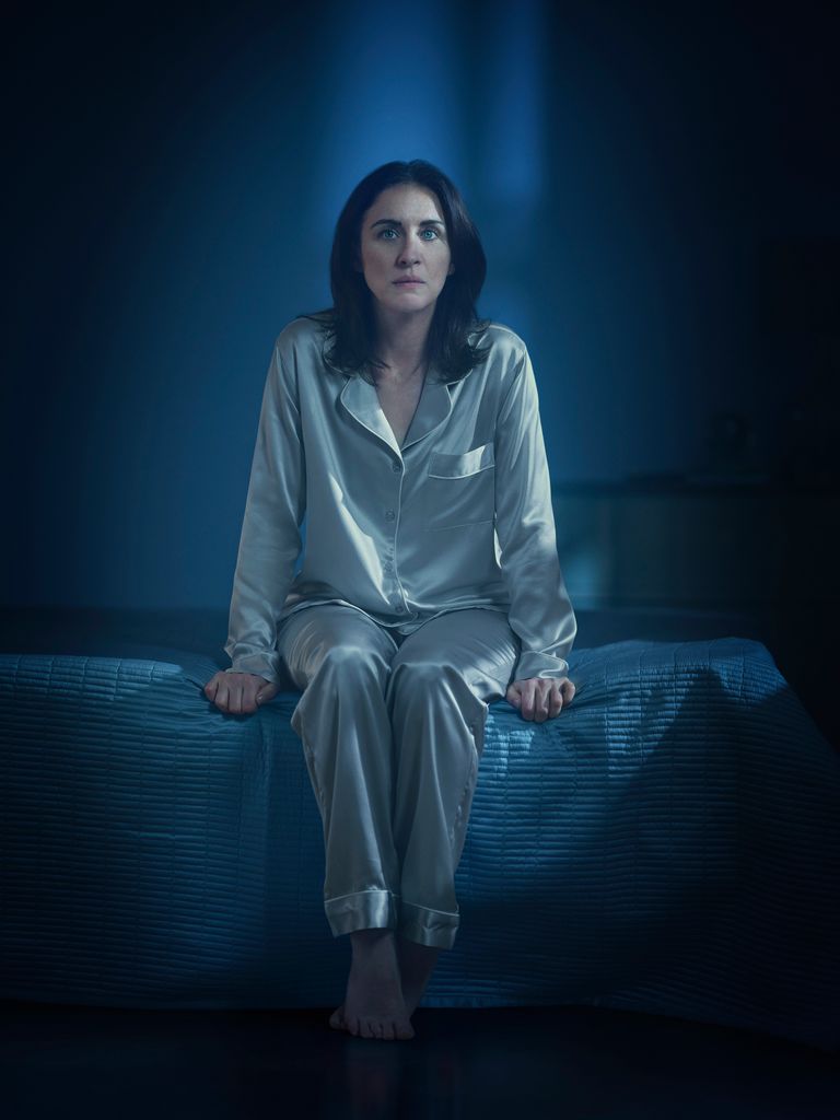 woman sitting on edge of bed in dark room