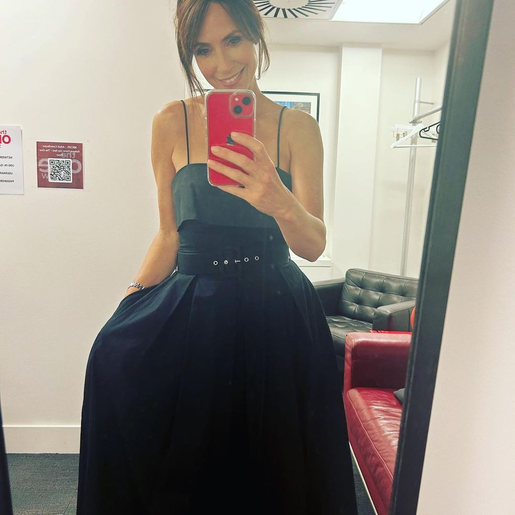 Alex Jones taking a selfie in a strappy black dress with a waist belt