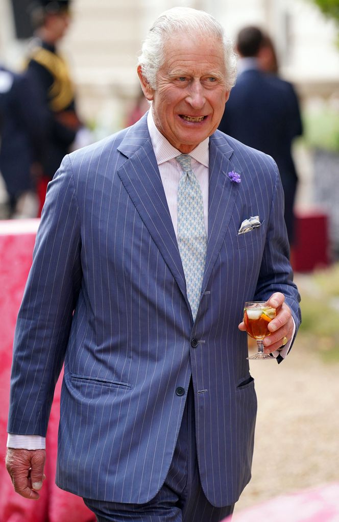 King Charles wears a pinstripe suit and carries a glass of Pimm's
