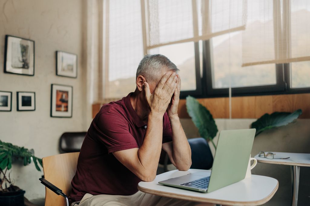 Tired mature man uses laptop