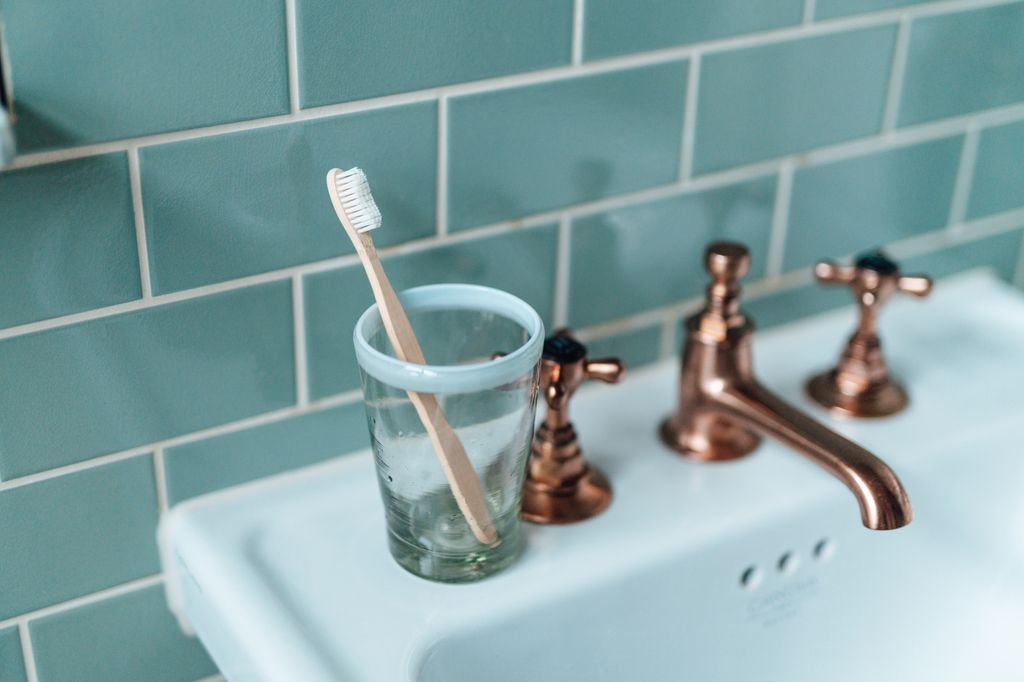 Plastic free wooden toothbrush in a glass cup on basin in bathroom