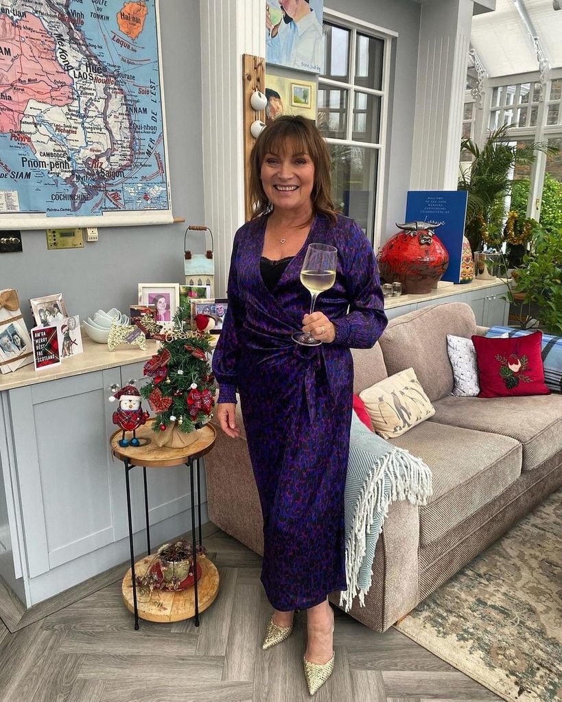Lorraine Kelly holds glass of wine wearing purple dress in conservatory