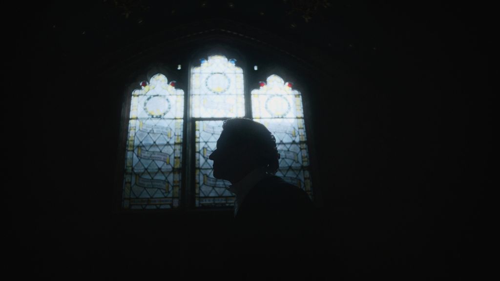 A shadowed image of a man standing by stained glass windows