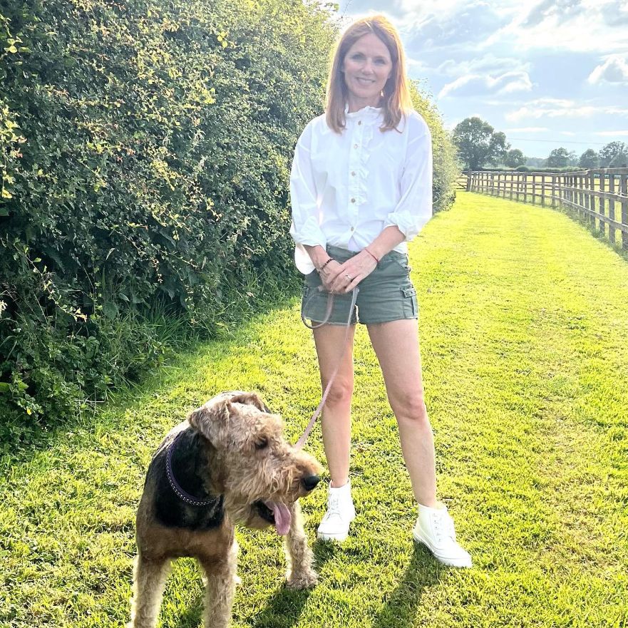 Geri Horner walking a dog while wearing a white buttoned shirt and green shorts