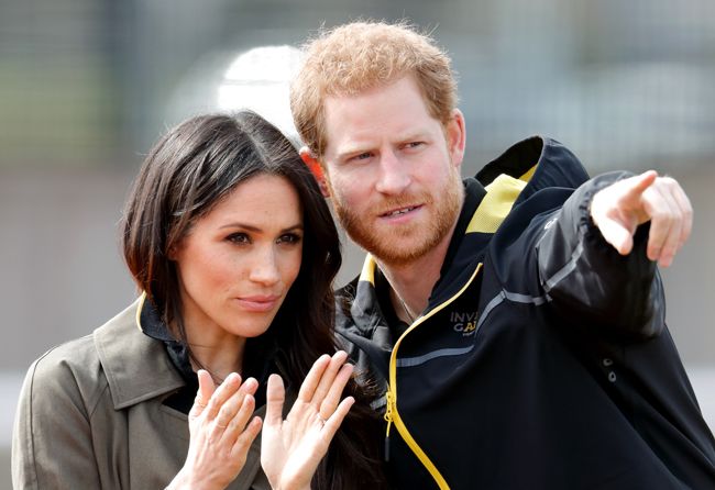 Meghan Markle and Prince Harry outside in coats, Prince Harry is pointing to something in the distance