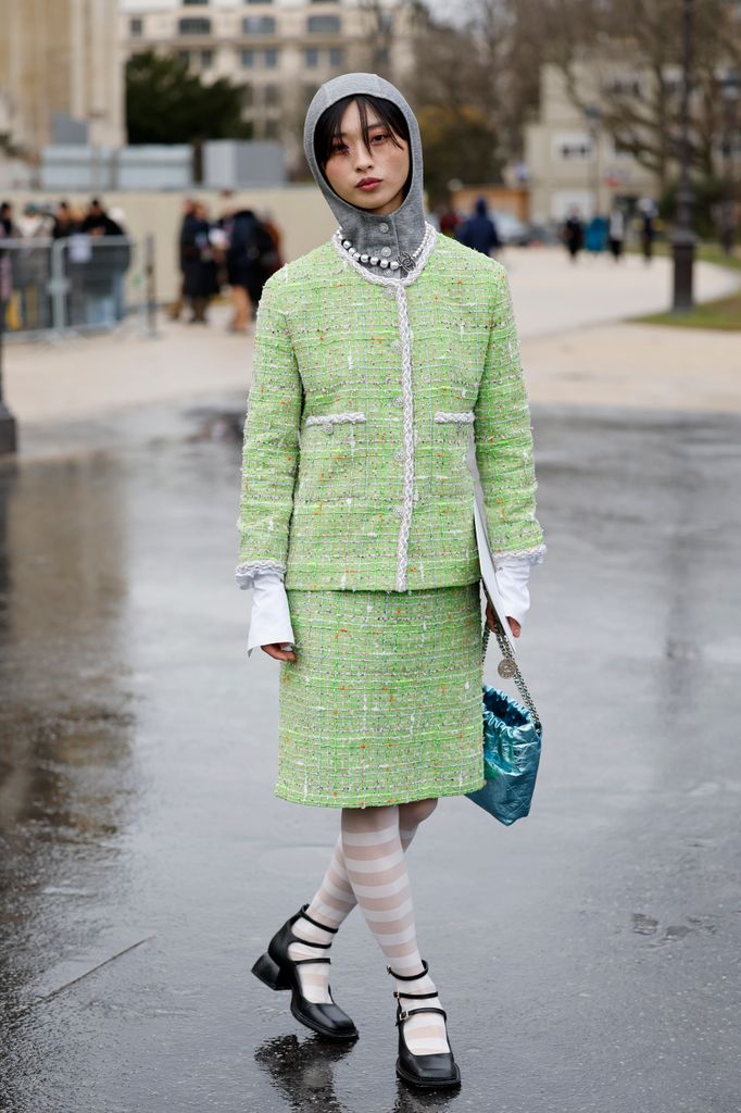 Yaqian Lan wears green tweed Chanel jacket with matching midi skirt, white shirt, grey jumper, metallic blue Chanel bag, white striped tights, black mary jane shoes, outside Chanel, during Haute Couture Spring-Summer 2025 as part of  Paris Fashion Week on January 28, 2025 in Paris, France.