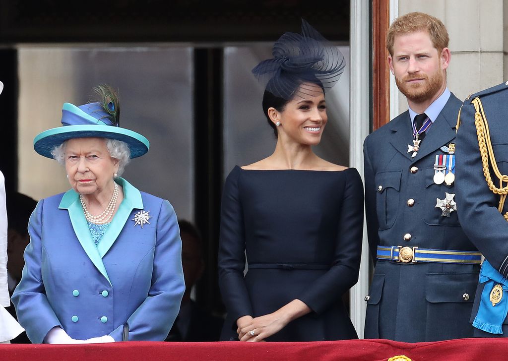 Queen Elizabeth II in a blue coat next to smiling Meghan Markle and Prince Harry