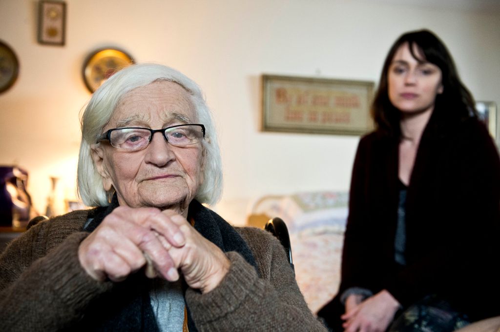 elderly woman sitting in chair, next to woman on bed