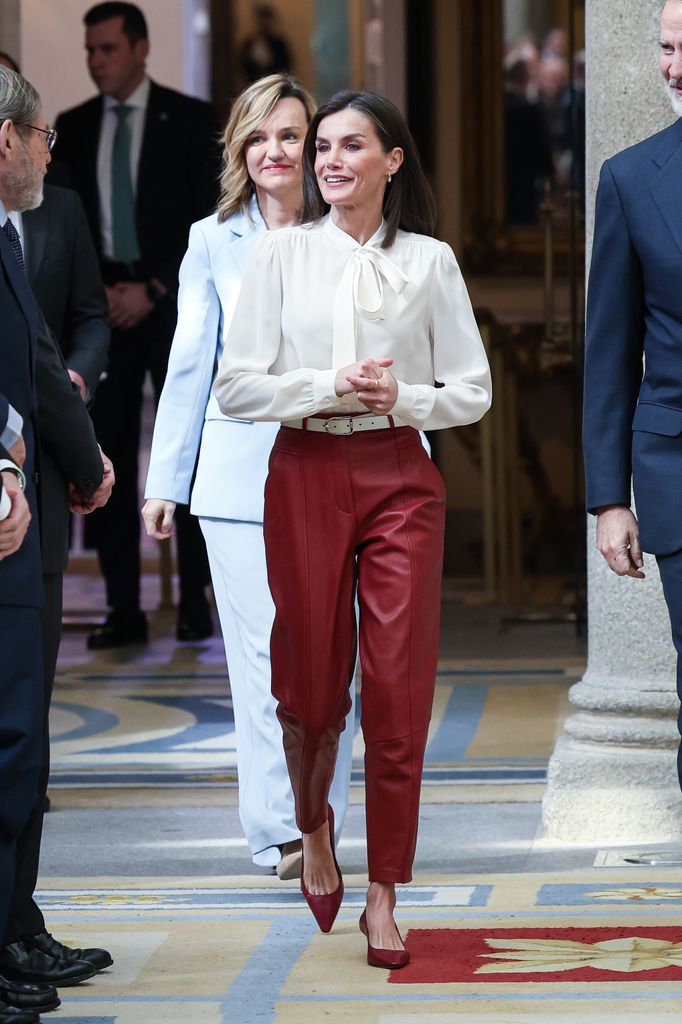 Queen Letizia of Spain walking and wearing red trousers, a white shirt and red heels