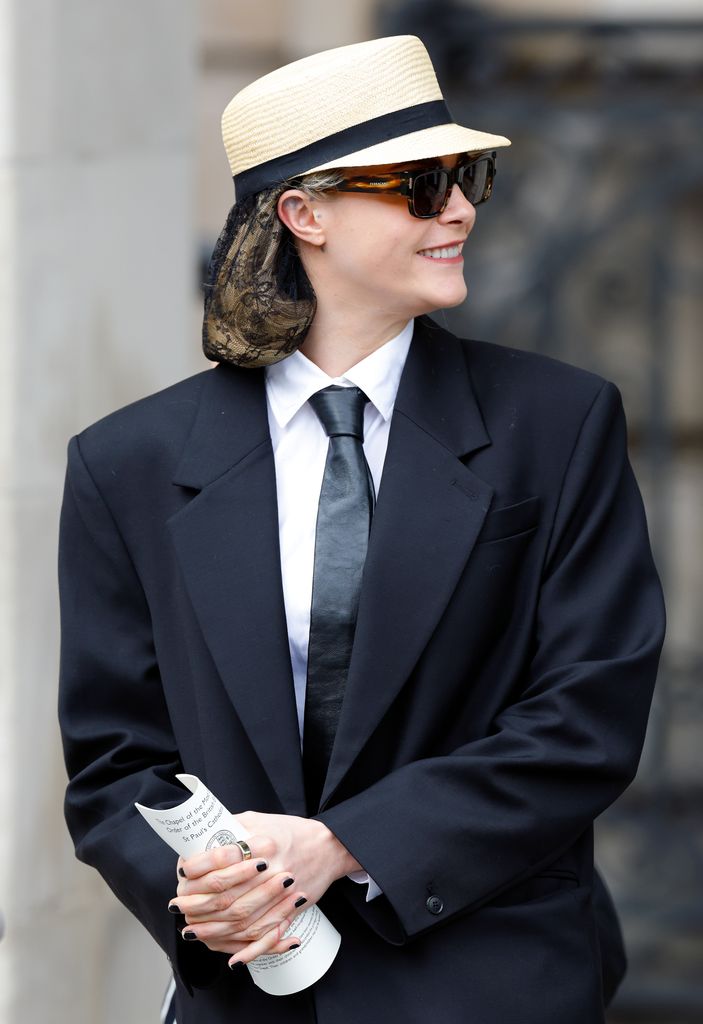 Cara Delevingne smiles to right in suit and sunglasses