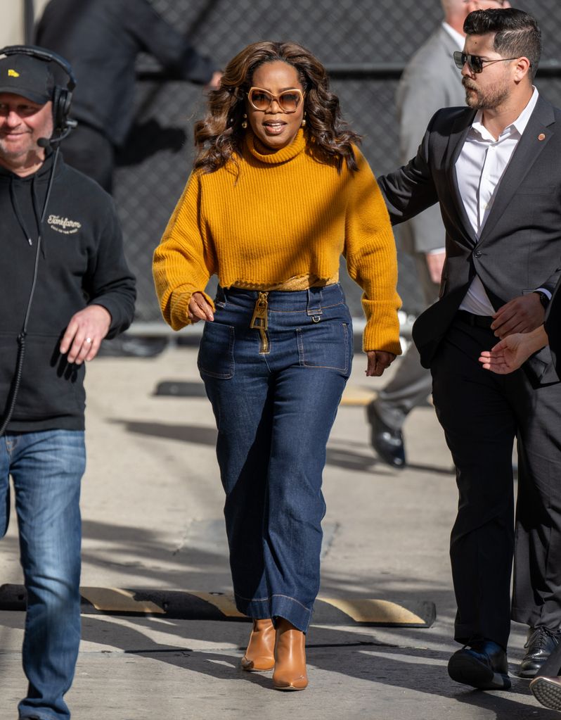 Oprah walking in jeans and mustard sweater
