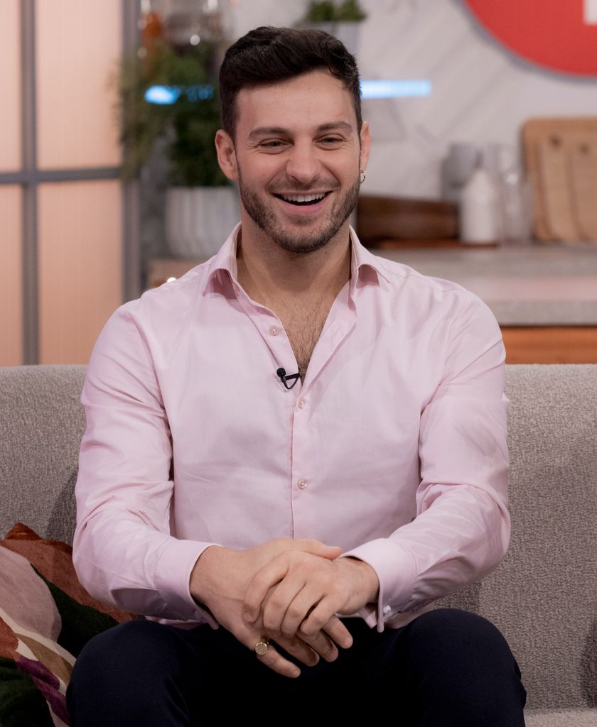 Vito Coppola sitting on a sofa in a pink shirt