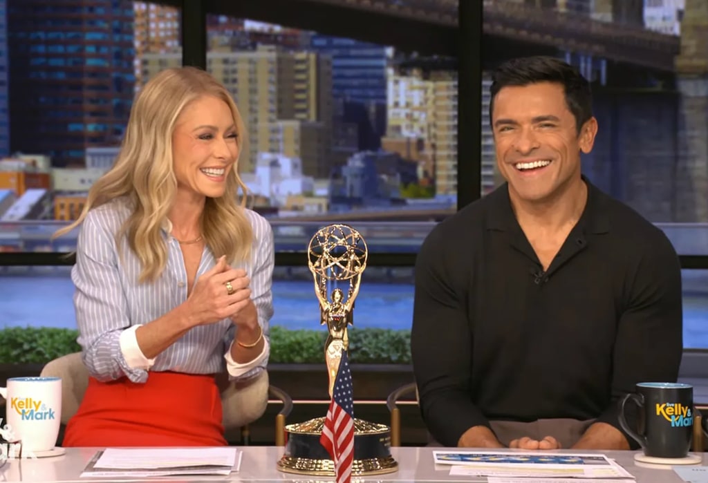 Kelly Ripa in blue shirt and red pants and Mark Consuelos in black shirt sat in studio