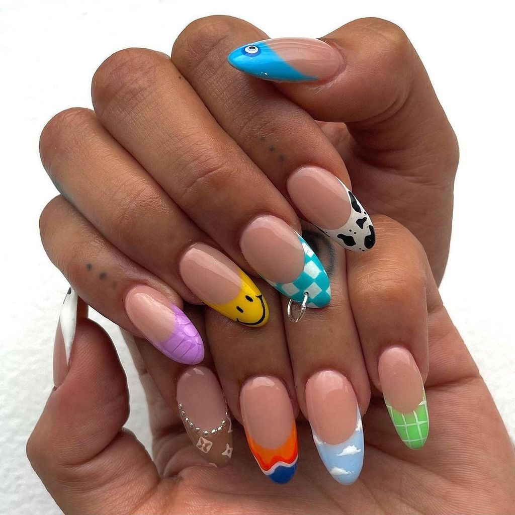 Almond nails with a variety of colorful designs on each finger, including smiley faces, patterns, and charms. This manicure exudes fun, creativity, and uniqueness, perfect for an eclectic vibe.